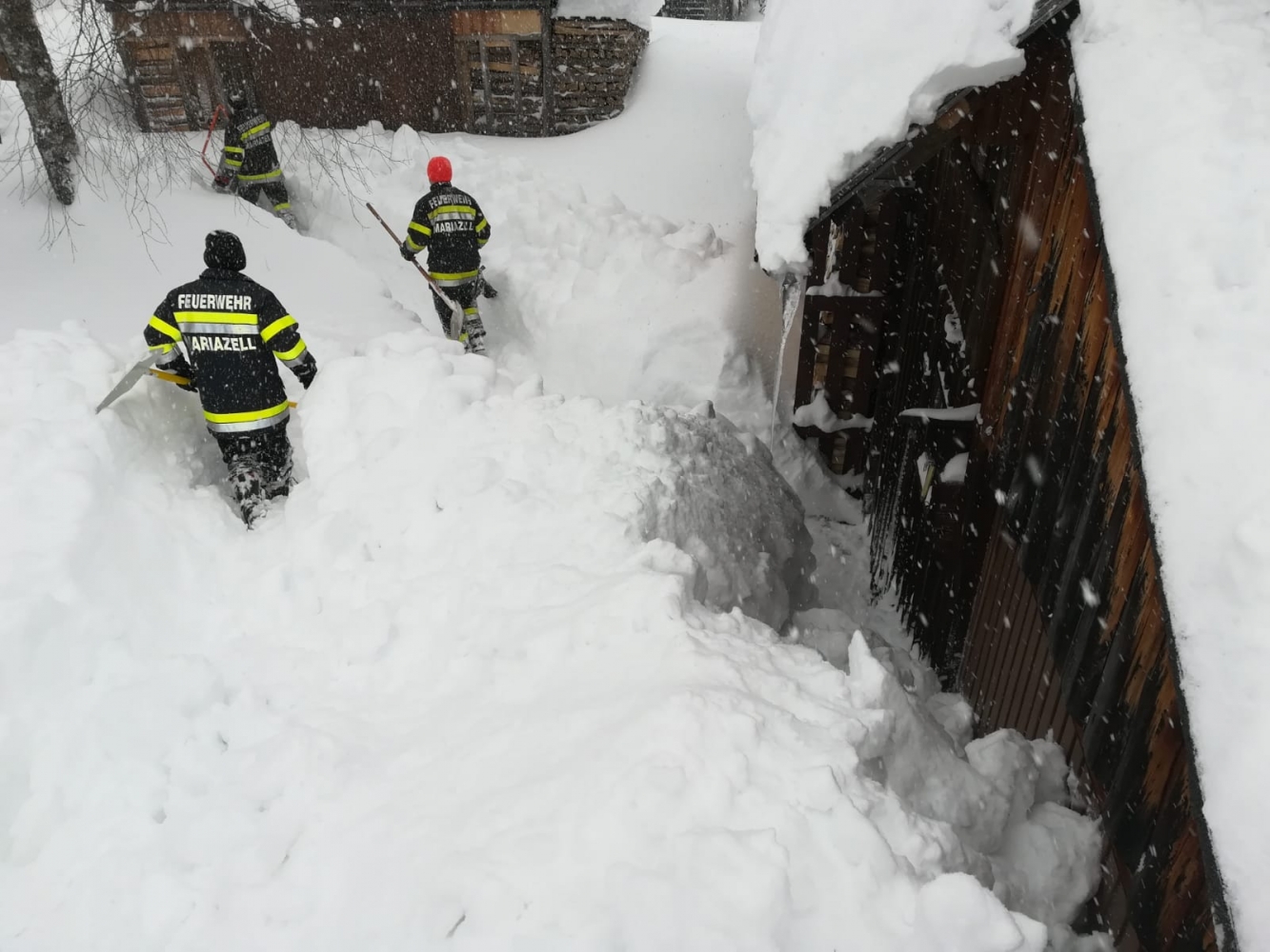 Einsatzkräfte schaufeln auf einem rießen Schneeberg vor einem Haus