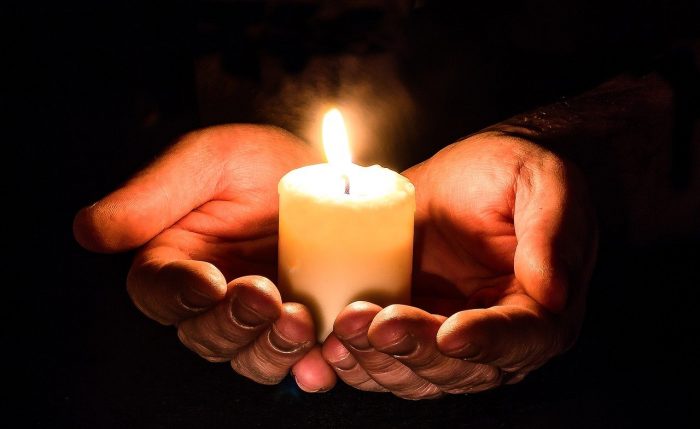 In zwei Händen befindet sich eine Kerze mit dem Friedenslicht aus Bethlehem