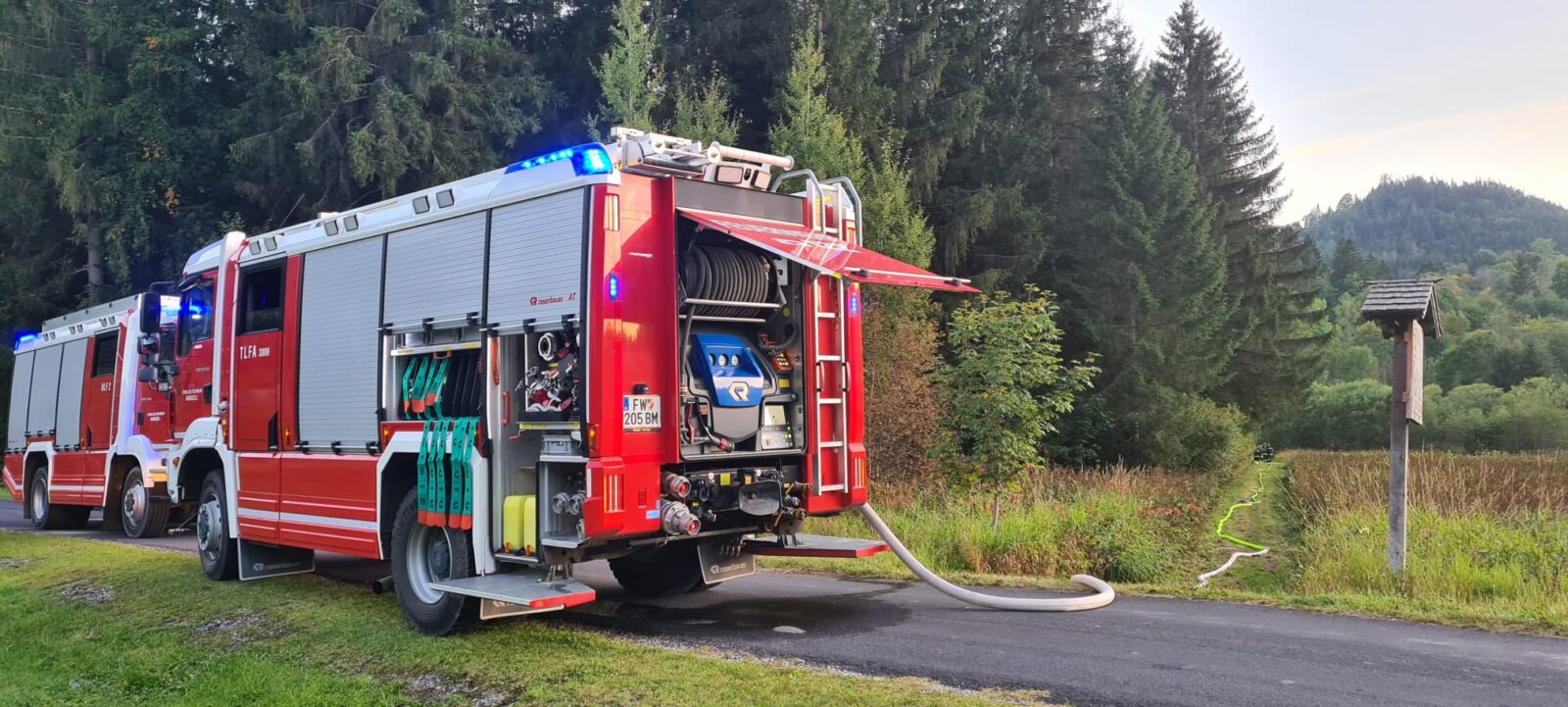 Zu sehen sind zwei Löschfahrzeuge neben einem Waldstück und sehr lange Löschleitungen.